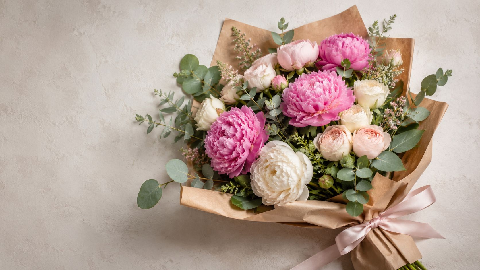 Un hermoso ramo de peonías frescas y rosas envuelto en papel artesanal con un lazo elegante.