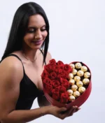 mujer sonriendo sosteniendo caja en forma de corazón con rosas y chocolates